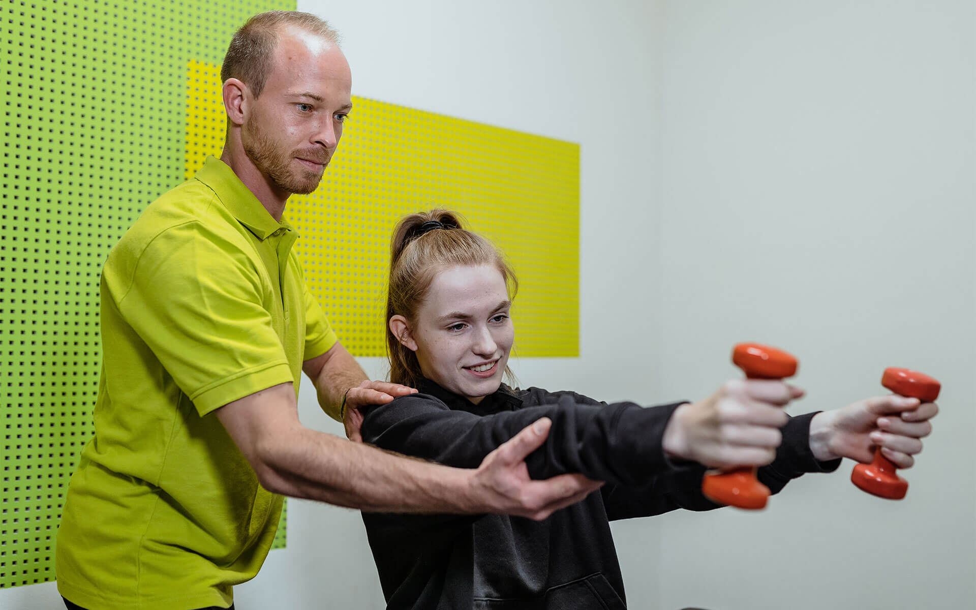 Therapeut hilft Patientin bei einem Training der Arme mit Gewichten