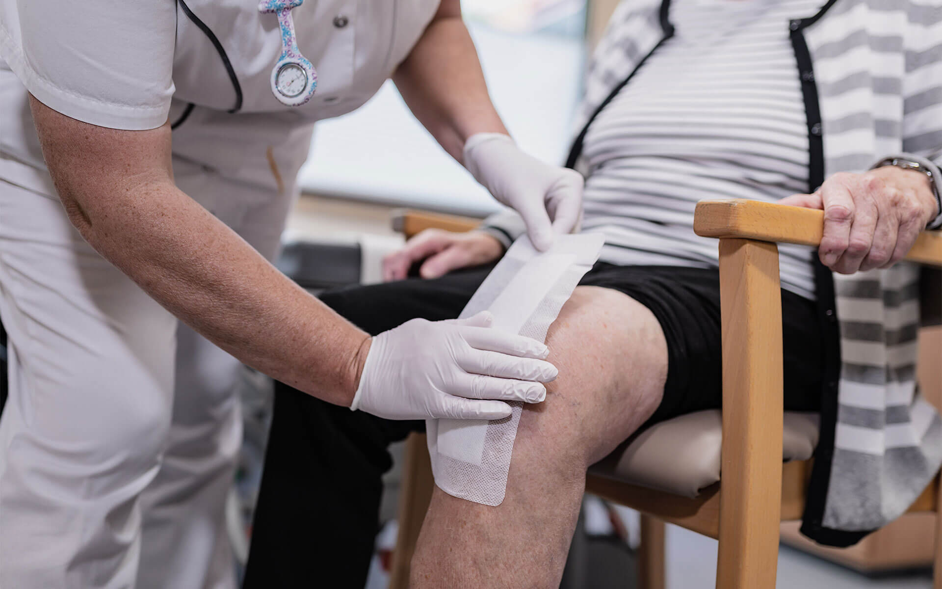 Pflegerin klebt Narbe am Knie mit einem Pflaster ab